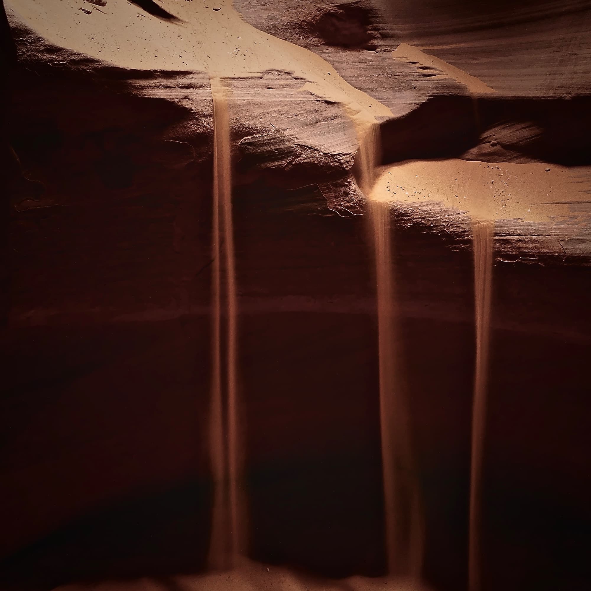 Fine sand falling down the dark walls of a slot canyon